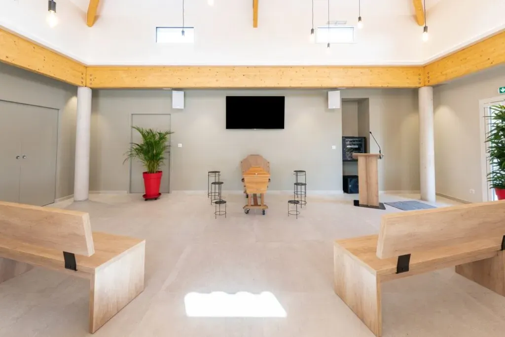 Grande salle de cérémonie funéraire avec bancs en bois, pupitre et écran.