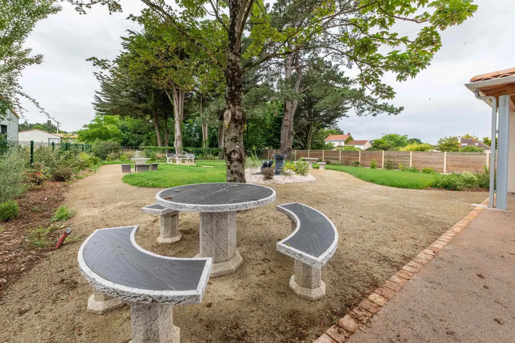 Espace vert extérieur aménagé avec bancs et tables en pierre pour le recueillement.